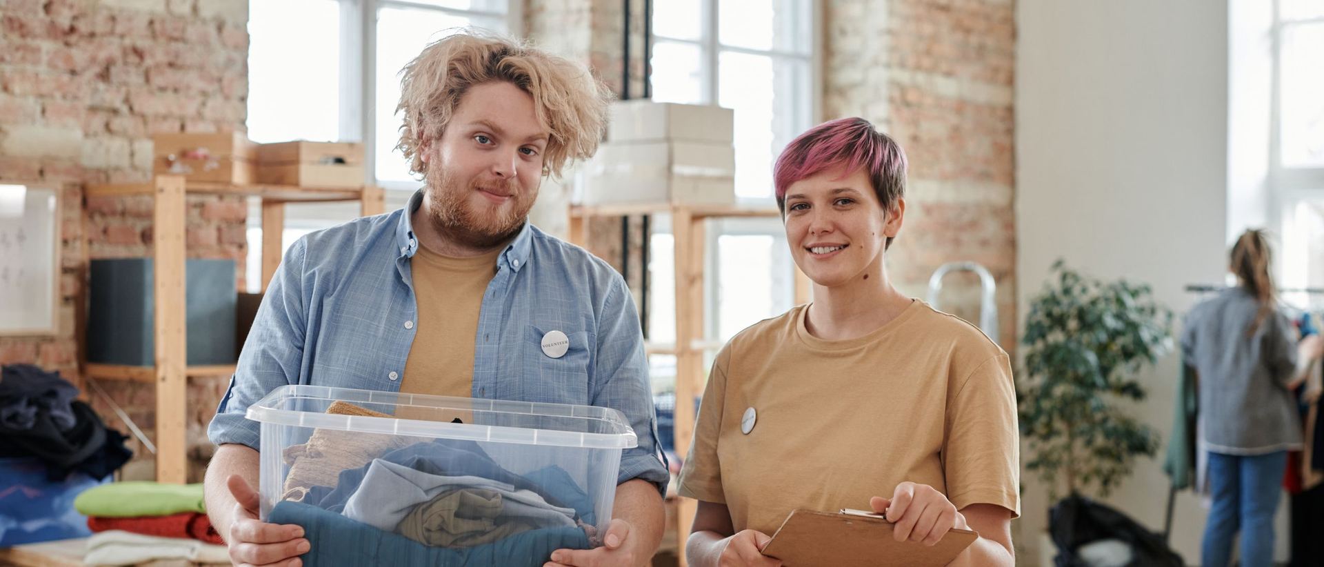 Two volunteers carrying a box of folded clothes at a community giving space