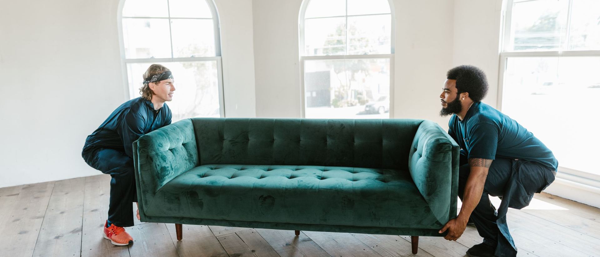 Two people carrying a green sofa together into a bright room