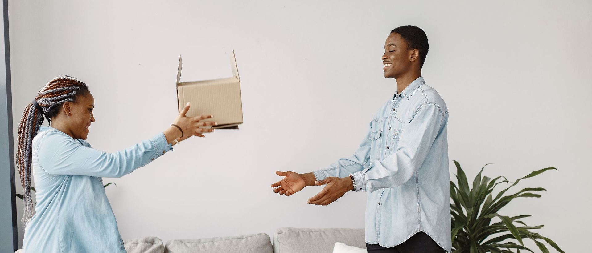 A woman handing a cardboard box of belongings to a smiling man in a living room